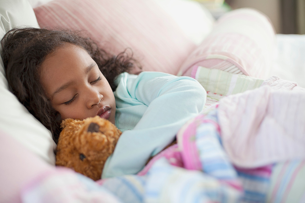 Child asleep with teddy bear in bed