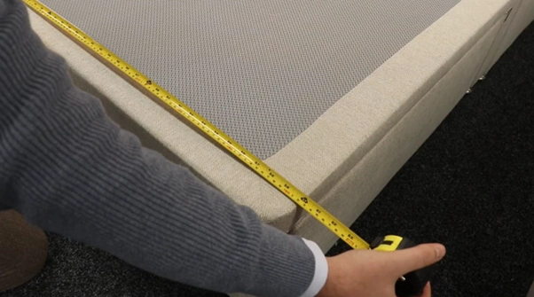An image of someone measuring a divan base with a tape measure