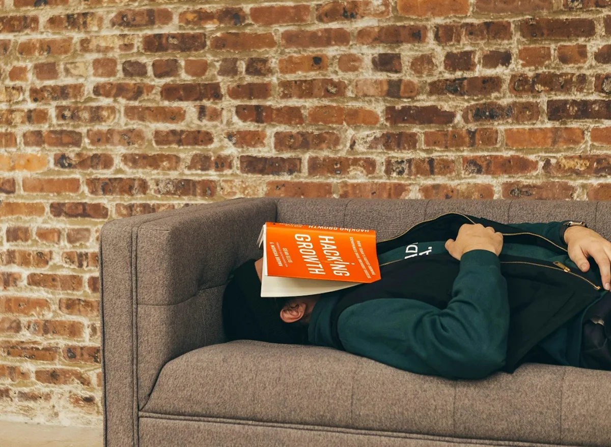 A student asleep laid on a sofa with a book covering his face